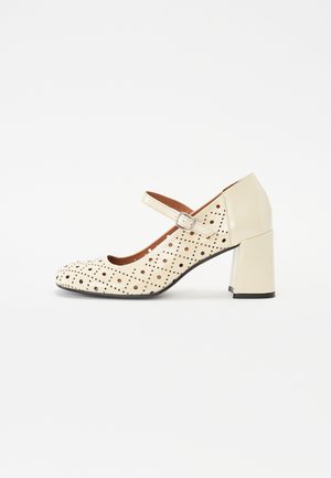 Kreemivärvi kingad perforatsiooni disainiga, Mary Jane rihmaga ja plokkninaga. Omab siledat tekstuuri ja kontrastset musta tallat.