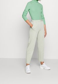 Maglione verde chiaro a collo alto e pantaloni su misura verde pallido, entrambi in un tessuto liscio, abbinati a sneakers bianche. Taglio semplice e moderno, con vestibilità rilassata.