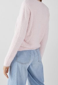 Pull en peluche rose avec un col rond et des manches longues, associé à un jean taille haute bleu clair avec une texture subtile et des poches arrière.