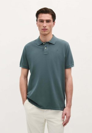 Poloshirt aus dunkelgrünem Baumwollstoff mit Kragen und einer Zwei-Knopf-Leiste. Kurze Ärmel, lockere Passform, dezentes Logo auf der Brust.