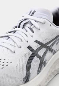 White athletic shoe with grey accents, featuring a mesh upper, textured detailing, flat laces, and a cushioned sole for comfort.