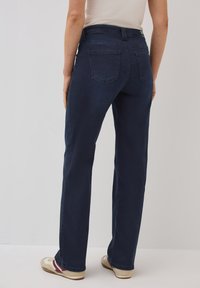 Jeans de mezclilla azul oscuro con un diseño de pierna recta, que cuentan con dos bolsillos traseros y una cintura de media altura, combinados con zapatos casuales beige.