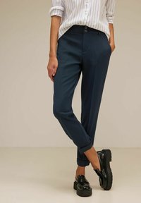 Námořnické kalhoty v úzkém střihu s texturovanou látkou, dvěma předními kapsami a ohrnutými nohavicemi, doplněné černými mokasínami.