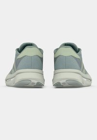 Ζευγάρι αθλητικών παπουτσιών σε ανοιχτό πράσινο και γκρι, εμφανιζόμενα από την πίσω όψη σε λευκό φόντο, με έμφαση στις μαλακές φτέρνες και τις υφασμένες σόλες.