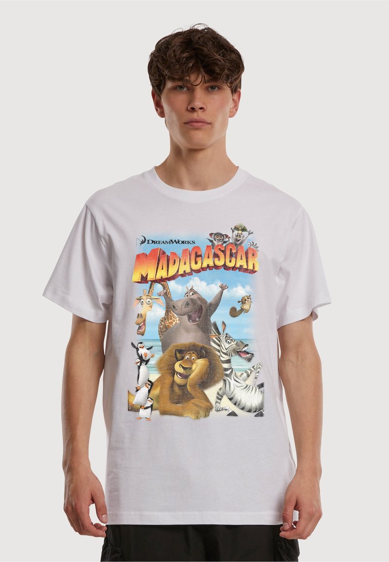 T-shirt blanc avec un motif coloré "Madagascar" représentant des personnages animés, dont des lions, des manchots et une girafe, sur un fond tropical.