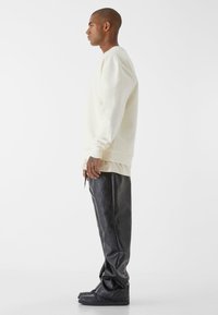Felpa color crema con maniche lunghe e polsini a coste, abbinata a pantaloni oversize in ecopelle neri e sneakers alte nere.