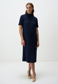 Abito midi blu navy con scollo alto, maniche corte, motivo testurizzato e silhouette dritta, abbinato a tacchi nudi.