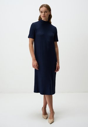 Abito midi blu navy con scollo alto, maniche corte, motivo testurizzato e silhouette dritta, abbinato a tacchi nudi.