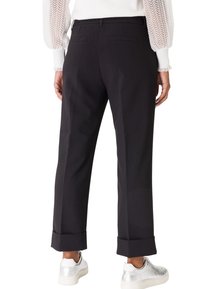Pantalons noirs ajustés avec une coupe décontractée, ourlet à revers et deux poches arrière. Portés avec un haut à manches blanches texturées et des baskets argentées.