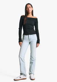 Črna rebrasta majica z dolgimi rokavi in odkrito ramo, kombinirana s svetloblue naravnost krojenimi džinsom in belimi supergami z rjavimi detajli.