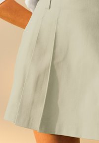 Jupe plissée vert clair en tissu texturé, dotée d'une coupe droite et d'un ourlet qui tombe au-dessus du genou, avec des détails de couture subtils.