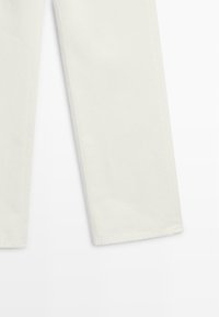 Vita denimbyxor med rak ben-design, synliga sömmar och ofärdig fåll. Tygtexturen verkar robust och lätt strukturerad.