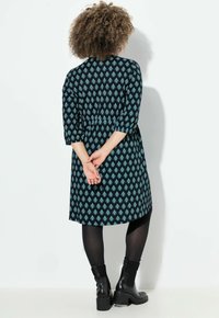 Musta mekko, jossa on teal-värisiä timantin kuvioita, kolmannen neljänneksen hihat, vyön sitominen vyötärölle ja leveä helma. Yhdistetty mustiin legginsseihin ja nilkkureihin.