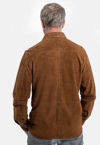 Braunes Wildlederhemd mit langen Ärmeln und einem Button-Down-Kragen. Es hat eine glatte Textur und eine Naht, die entlang der Mitte des Rückens verläuft.