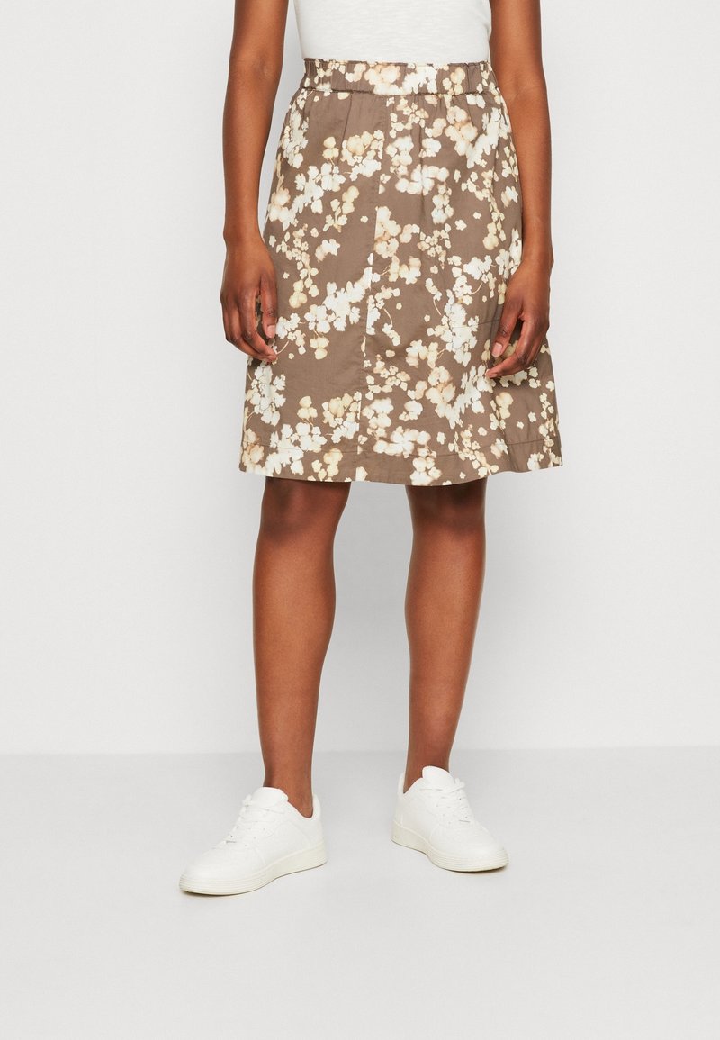 Gonna floreale marrone con vita elastica, lunghezza al ginocchio, caratterizzata da motivi floreali bianchi e crema, abbinata a sneakers bianche.