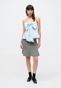 Jasnoniebieski top bez rękawów z dużą kokardą z przodu, zestawiony z szarą rozkloszowaną spódnicą. Modelka ma na sobie czarne skarpetki i buty.