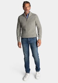 Lichtgrijze gebreide pullover met een halve rits hals, gecombineerd met blauwe jeans en witte sneakers. De pullover heeft een ribbeltextuur en een casual pasvorm.