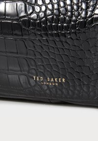 Bolso negro con estampado de cocodrilo y acabado brillante, con la marca dorada "TED BAKER LONDON". Elegante forma rectangular.