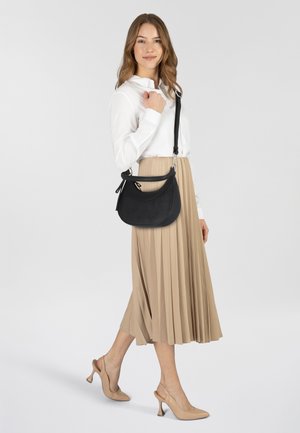 Borsa a tracolla in pelle nera con forma curva e accessori in argento, indossata sopra una gonna midi beige plissettata e una maglietta bianca.