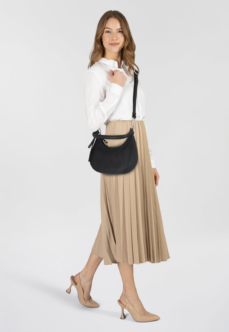 Borsa a tracolla in pelle nera con forma curva e accessori in argento, indossata sopra una gonna midi beige plissettata e una maglietta bianca.