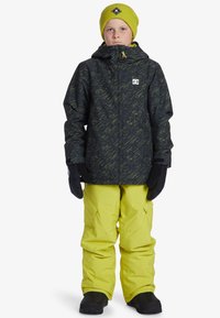 Svart mönstrad jacka med gula accenter, gula snöbyxor, svarta handskar och en ljusgrön mössa. Enkel design, funktionell för vintern.