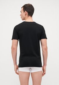 T-shirt nera a maniche corte in tessuto di cotone liscio, con colletto girocollo classico e forma aderente, vista da dietro.