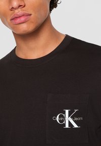 Zwarte katoenen t-shirt met een ronde hals en een linkse borstzak met een wit "CK" logo en merknaam gedrukt.
