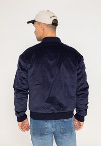 Veste bomber en velours côtelé bleu marine avec des poignets et un col côtelés, présentant des détails brodés aux épaules et une texture lisse.