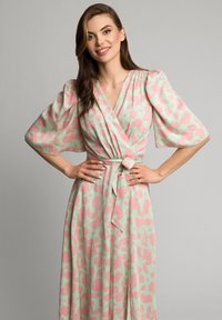 Sukienka maxi w kwiatowy wzór z miętowym tłem i różowymi kwiatami. Posiada fason kopertowy z szerokimi rękawami i wiązaniem w talii.