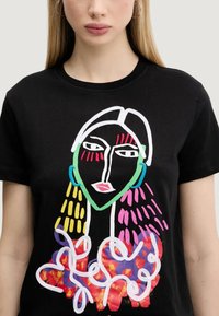 T-shirt nera in cotone con una stampa astratta colorata di un volto con accenti verdi, occhi rossi e capelli a fantasia in rosa e giallo.