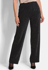 Zwarte wijde broek met een glanzende afwerking, voorzien van een elastische tailleband en een soepele textuur, gecombineerd met zwarte hakken.