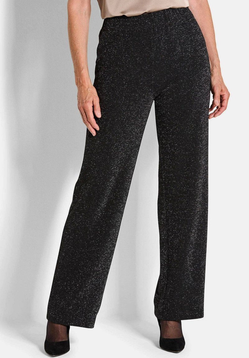 Zwarte wijde broek met een glanzende afwerking, voorzien van een elastische tailleband en een soepele textuur, gecombineerd met zwarte hakken.