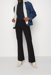 Džínová bunda s bílým umělým kožíškem na límci, námořnický rolák s puntíky, černé rozšířené kalhoty a béžové kotníkové boty na robustním podpatku.