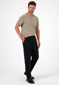 Beige trui met korte mouwen, gecombineerd met zwarte broeken. De outfit wordt aangevuld met stijlvolle zwarte schoenen, wat zorgt voor een verzorgde uitstraling.