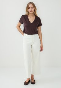 T-shirt marrone a V, pantaloni bianchi a gamba larga, ballerine nere intrecciate. Design semplice, tessuto morbido, colori naturali, silhouette dritta.