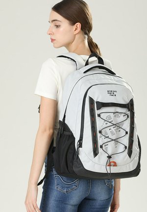 Gray and black backpack with mesh side pockets, adjustable straps, and front bungee cord design. Made of durable material, lightweight.
