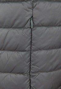 Primer plano de una chaqueta acolchada gris con costuras acolchadas horizontales y un pequeño lazo de tela en la costura central.