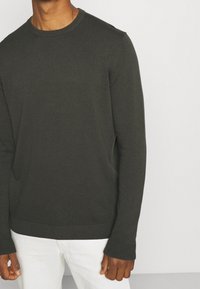 Pull vert foncé en maille à manches longues avec un col rond. Présente des poignets et un ourlet côtelés, fabriqué en tissu doux et texturé.