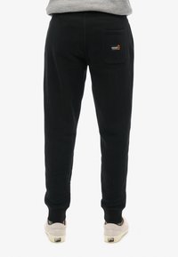 Zwarte joggingsbroek met een strakke pasvorm, voorzien van een achterzak en een klein logo-patch. Gemaakt van een zachte, rekbare stof.