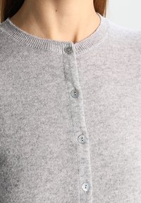 Grå stickad kofta med rund halsringning, knäppning med metallknappar och en mjuk textur som passar bra för lager på lager.