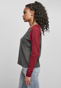 Grau und rotes Langarmshirt mit Rundhalsausschnitt und Raglanärmeln; weicher Stoff und lockere Passform. Kombiniert mit hellblauen Jeans.
