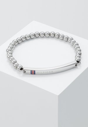 Bracelet à perles argentées avec une plaque rectangulaire poli arborant des rayures rouges, blanches et bleues ainsi que la gravure "HILFIGER".