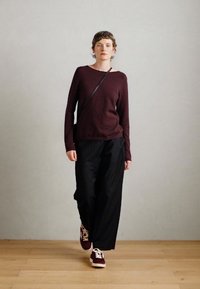Tamno burgundska дugački rukav džemper, labave crne hlače i burgundske patike. Jednostavan dizajn s ležernim krojem i minimalističkim stilom.