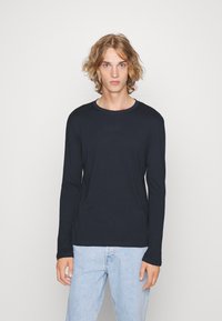 Svart langermet t-skjorte i myk bomull, rund hals, vanlig passform, vist på en modell som har på seg lyseblå jeans. Enkel design, ingen mønstre.