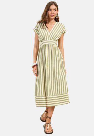 Naine kannab varrukateta rohevalgeid vertikaalse triibuga midi-pikka kleiti, millel on V-kaelus ja sandaalid, millel on valged ümarad detailid.