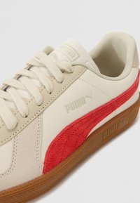 Adidași Puma cu partea superioară din piele crem, accent de suede roșu și talpă din cauciuc bej. Dispune de închidere cu șireturi și logo branduit.