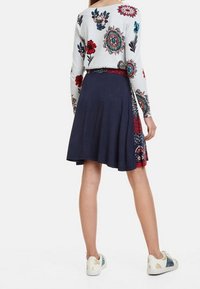 Blommig långärmad topp i ljusgrått med färgglad broderi, kombinerad med en marinblå knä-lång kjol med mönster och en midjebandaccent.