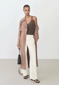 Brown suede trench coat over a brown tank top, white wide-leg pants, and black handbag. Smooth textures and neutral color palette.