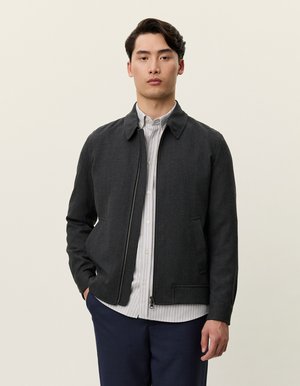 Mørk grå jakke med krage, frontglidelås og to sidelommer. Brukt over en lys stripete skjorte og paret med marineblå bukser.