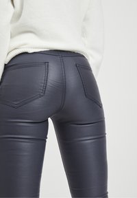 Leggings ajustados de color azul marino, hechos de un material brillante, que presentan costuras decorativas y dos bolsillos traseros con solapas puntiagudas.